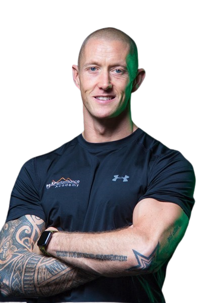 A man with a shaved head and tattoos on his arms is wearing a black t-shirt with the logo "Performance Academy." He is smiling and has his arms crossed. He is also wearing a smartwatch. The background is transparent.